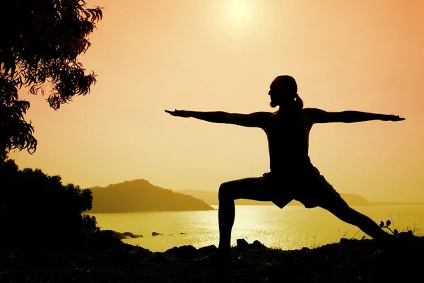 Man doing yoga pose warrior pose II at sunset